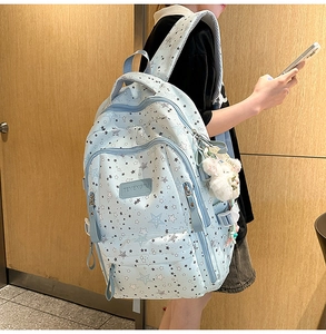 Close-up of light blue star print backpack with cute plush bear keychain and logo detail