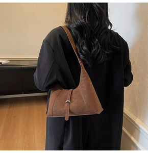Close-up of brown suede crescent shoulder bag with metallic buckle detail on model