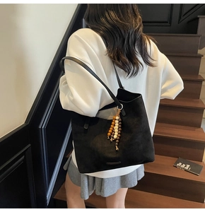 Back view of a model carrying a black suede tote bag with a colorful beaded tassel charm