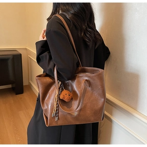 Detailed close-up of dark brown leather tote bag with plush bear charm and tassel