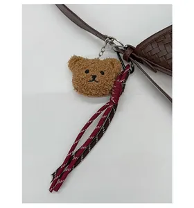 Detail of brown teddy bear plush pendant with red woven cord on a woven leather bag