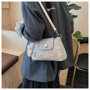 Detalle de bolso gris con parches decorativos y colgante de peluche sobre una chaqueta