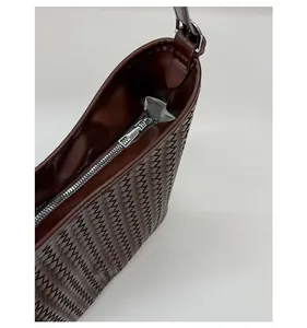 Close-up of smooth metal zipper and woven leather texture on dark brown bucket bag