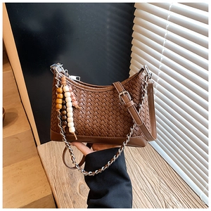 Detailed close-up of dark brown woven handbag with silver chain and beaded charm decoration