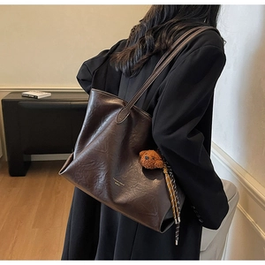 Detail of dark brown leather tote bag with plush bear charm and fashion lettering
