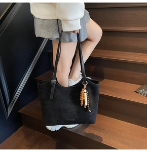 Detailed view of black suede tote bag with colorful beaded charm on a wooden staircase
