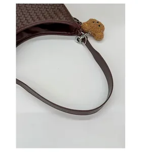 Detail of hand-woven dark brown bucket bag with smooth leather strap and plush bear charm