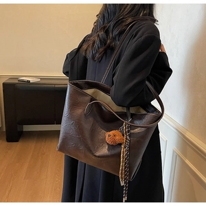 Detail view of large dark brown tote bag with cute plush bear charm on model's shoulder