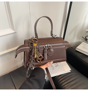 Close-up of brown matte faux leather handbag with dual metal zippers and creative charms
