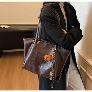 Detail of dark brown tote bag with plush teddy bear charm and woven tassel decoration