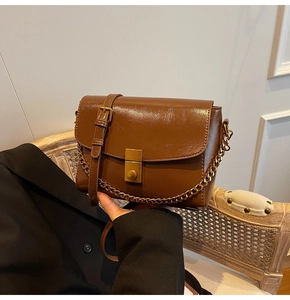 Détail d'un sac en similicuir marron brillant avec chaîne dorée et fermoir rotatif vintage