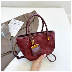 Detail of burgundy velvet bucket bag with gold hardware ring and mini charm on white background