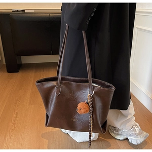 Detailed view of dark brown leather tote with embossed logo and plush bear pendant