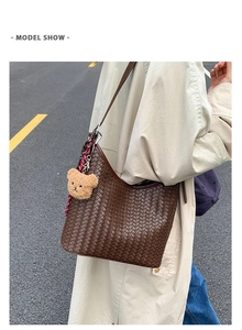 Detailed view of brown woven hobo bag with teddy bear charm on model's shoulder