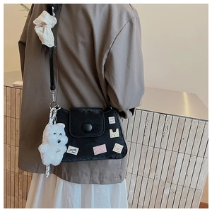 Detalle de bolso de hombro en ante negro con parches bordados y colgante de peluche blanco