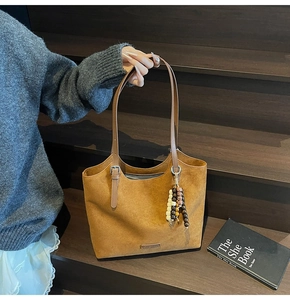 Detail of a brown suede tote bag with ethnic beaded charm and metallic logo on the side