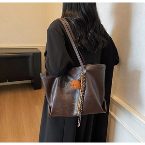 Detail of dark brown oil-wax leather tote bag with plush bear charm on a female model