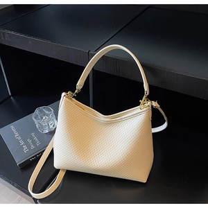 Détail d'un sac cabas tissé beige avec garnitures dorées posé sur un meuble noir élégant