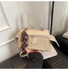 Detail of beige leather pillow bag featuring dual zippers and metal key charm