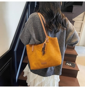 Detail of suede tote bag featuring a textured finish and vintage bead pendant accessory