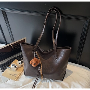 Detail of dark brown oil wax leather tote bag with poodle plush charm and striped straps