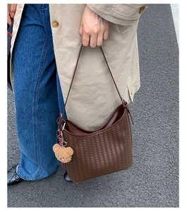 Detail of dark brown woven leather bucket bag featuring a cute plush bear pendant