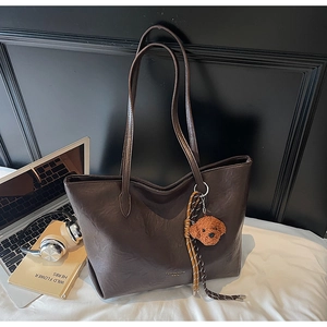 Detail of dark brown tote bag with V-shape texture, teddy charm and braided tassel detail