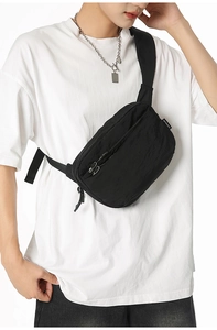 Detail of minimalist black nylon crossbody bag with dual zippers worn on white t-shirt