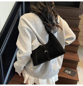 Detailed view of black suede shoulder bag with silver buckle worn on model's shoulder