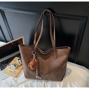 Close-up of brown PU leather tote bag with plush puppy pendant and woven tassel detail