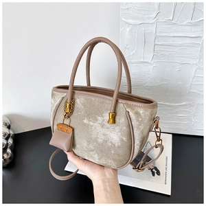 Close-up of velvet tote bag with golden metal buckles and a mini bag charm detail