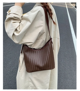 Close-up of brown woven texture hobo bag worn with a beige trench coat on a city street