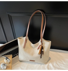 Close-up of beige suede tote bag texture with brown straps and wooden bead tassel detail