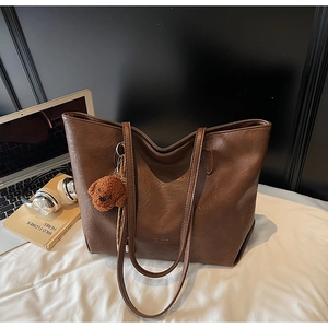 Detail of a large brown tote bag with leather texture and cute bear charm on a white cloth