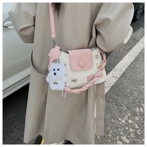 Detalle de bolso tipo cubo rosa y beige con dije de perro de peluche y correas para el hombro