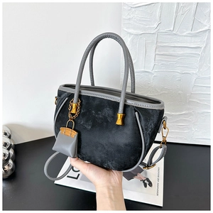 Close-up of black suede tote bag featuring grey leather handles and gold metal accents