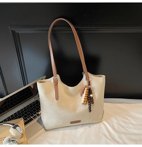 Detail view of beige suede tote bag featuring brown leather straps and wooden bead tassel