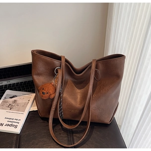 Detail of dark brown faux leather tote bag with vintage texture and plush bear charm
