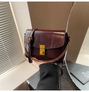 Détail du sac carré bordeaux à texture crocodile avec boucle dorée et bandoulière chaîne