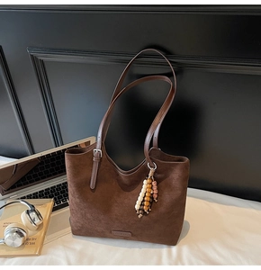 Detail of dark brown suede tote bag featuring leather strap and colorful wood bead tassel