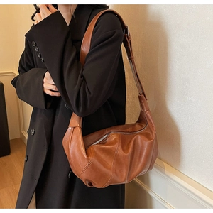 Detail of caramel brown leather crescent bag showing natural texture and wide strap