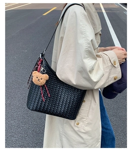 Detail of hand-woven black bucket bag with a cute brown bear charm on street style model