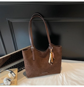 Detail of suede tote bag showing ethnic beads pendant and fine logo patch on brown leather