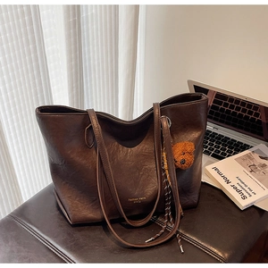 Detail of a large brown leather tote bag with a gold logo and cute plush bear charm