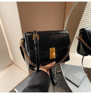 Détail d'un sac bandoulière en cuir verni noir avec chaîne dorée et fermoir carré en métal
