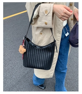 Outdoor street style view of black woven hobo shoulder bag with cute bear charm detail