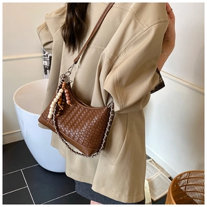 Detail of a brown woven hobo bag featuring silver chain strap and beaded tassel charms