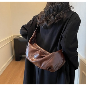 Brown hobo shoulder bag with pleated texture shown on a model in a minimalist room