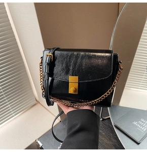 Gros plan du sac en cuir huilé noir avec fermoir à poussoir doré et bandoulière chaîne