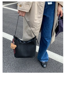Detail of black woven hobo bag with a cute bear charm, styled on a casual street outfit